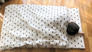 ブログ「モノオス」ディモアのベアマスクおひるねふとんセット（筒形バッグ）で、敷き・掛け両方がクロクマのふとんに子供が寝ている画像